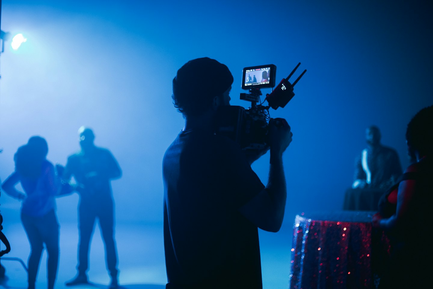 Videographer films silhouetted figures in a studio.