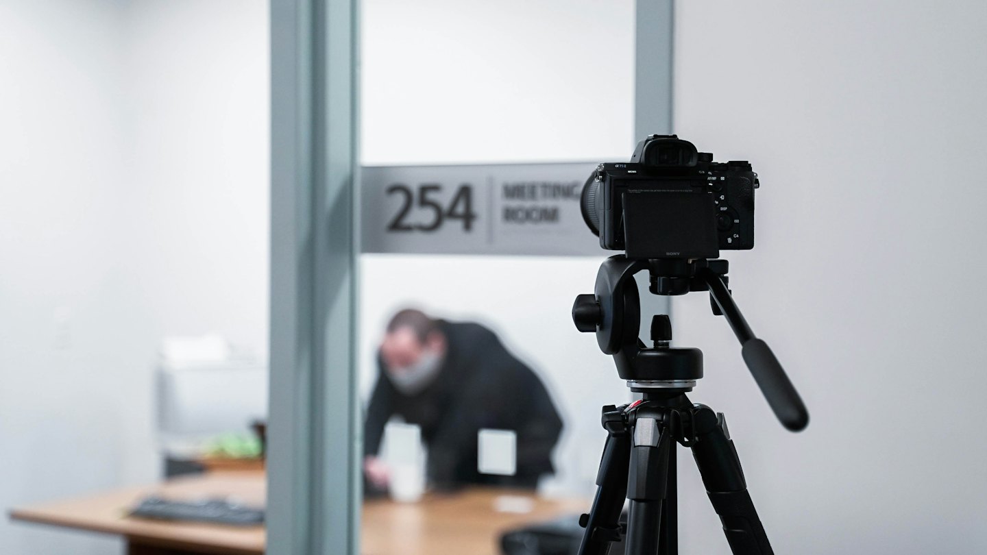 Camera on tripod recording a meeting room with a person at a table.