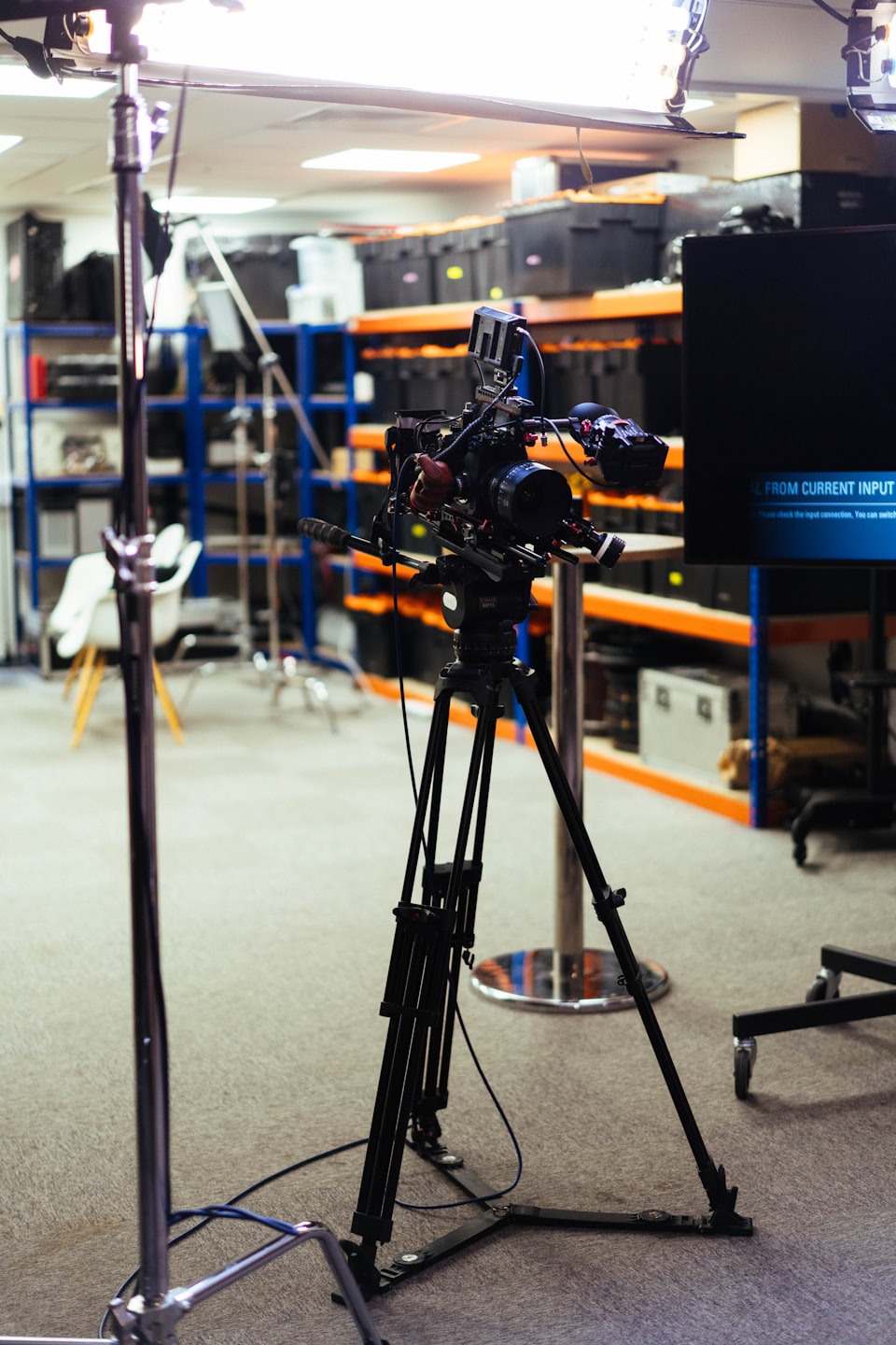 Professional video camera on a tripod inside a equipment warehouse.
